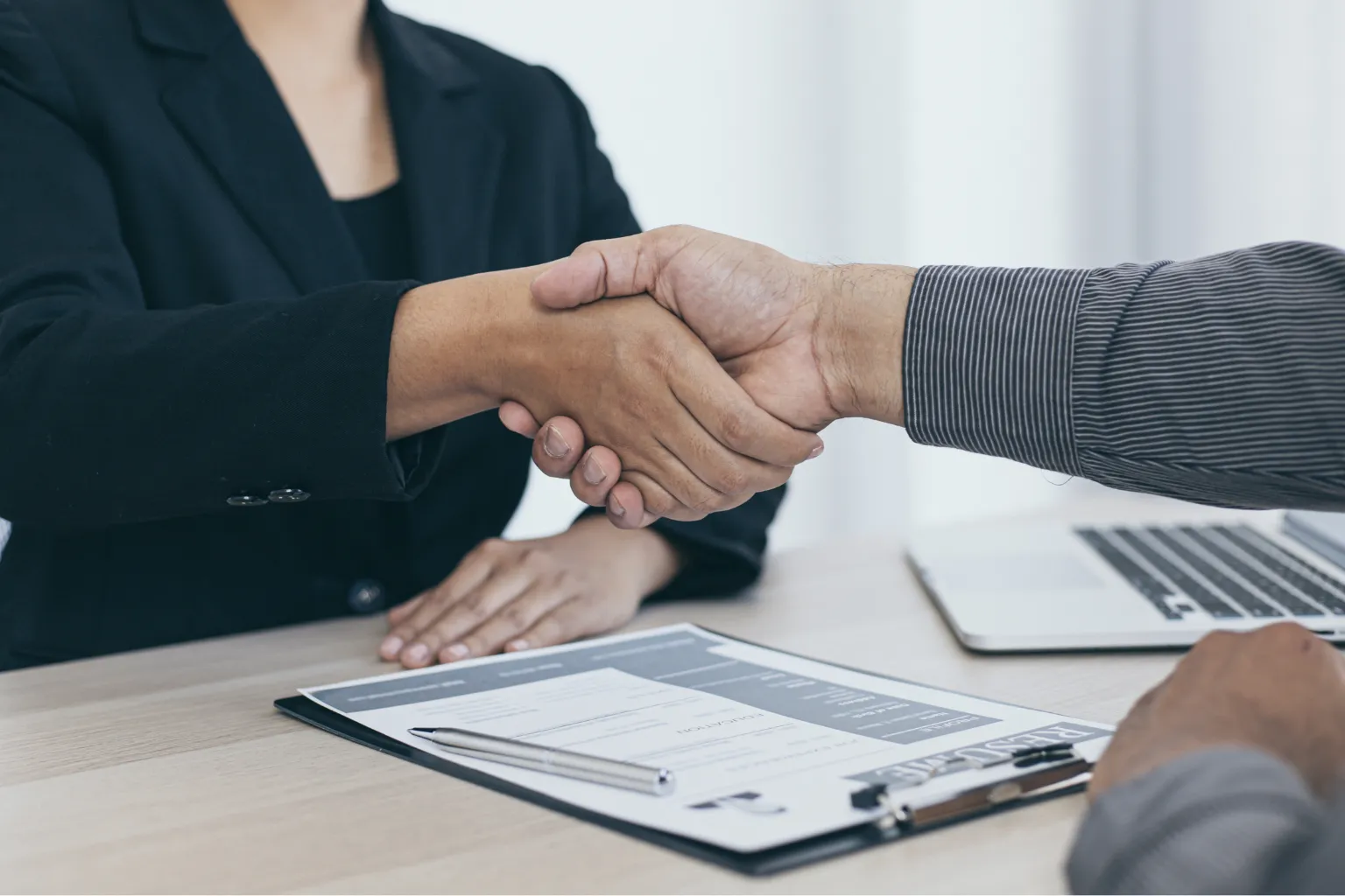 Two professionals shaking hands over a desk during an MBA interview.