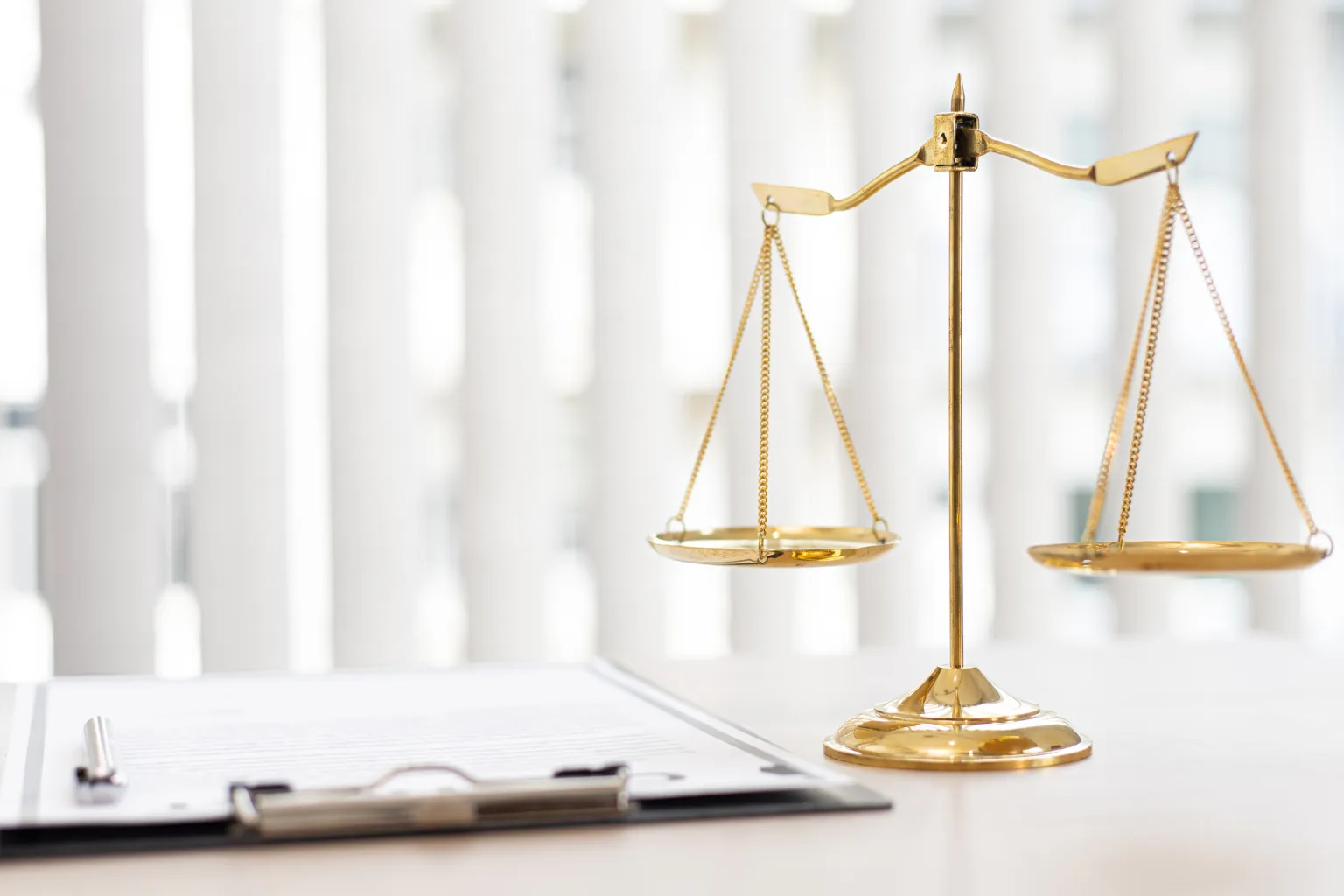 Law essay topics inspiration: gold scales, pen, and paper on desk.