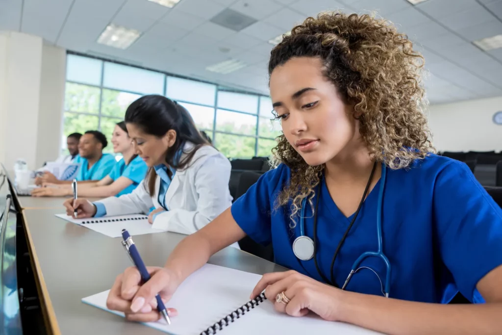 A diverse group of medical students attentively listening and taking notes in a classroom on how to write a nursing essay